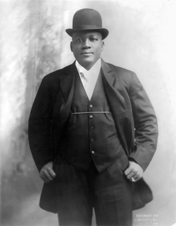 Jack Johnson "The Galveston Giant", posing for the camera in an elegant suit and bowler.